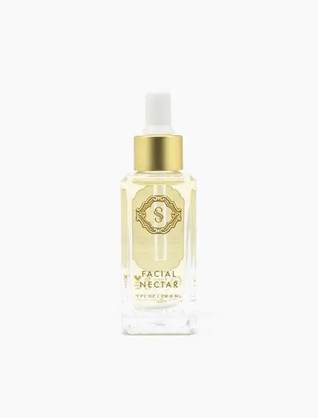 A bottle of facial serum with gold label.