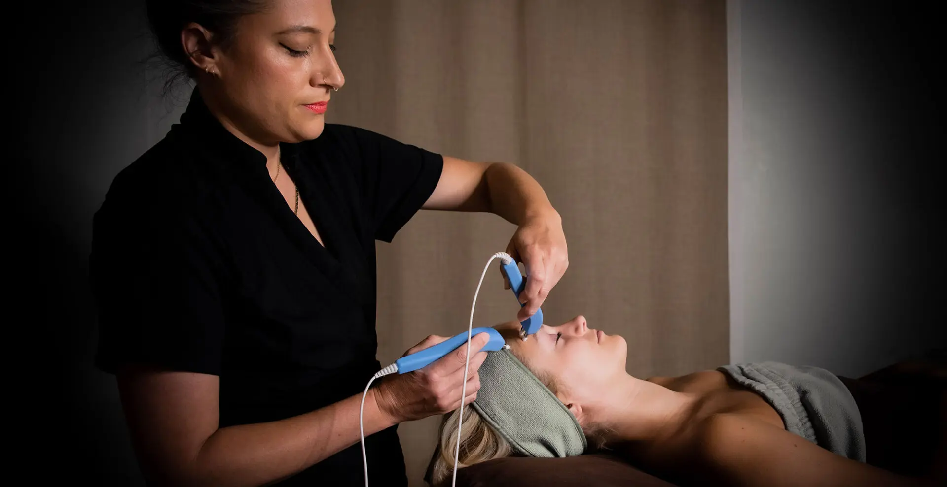 A woman is using an electric device to treat a patient 's face.