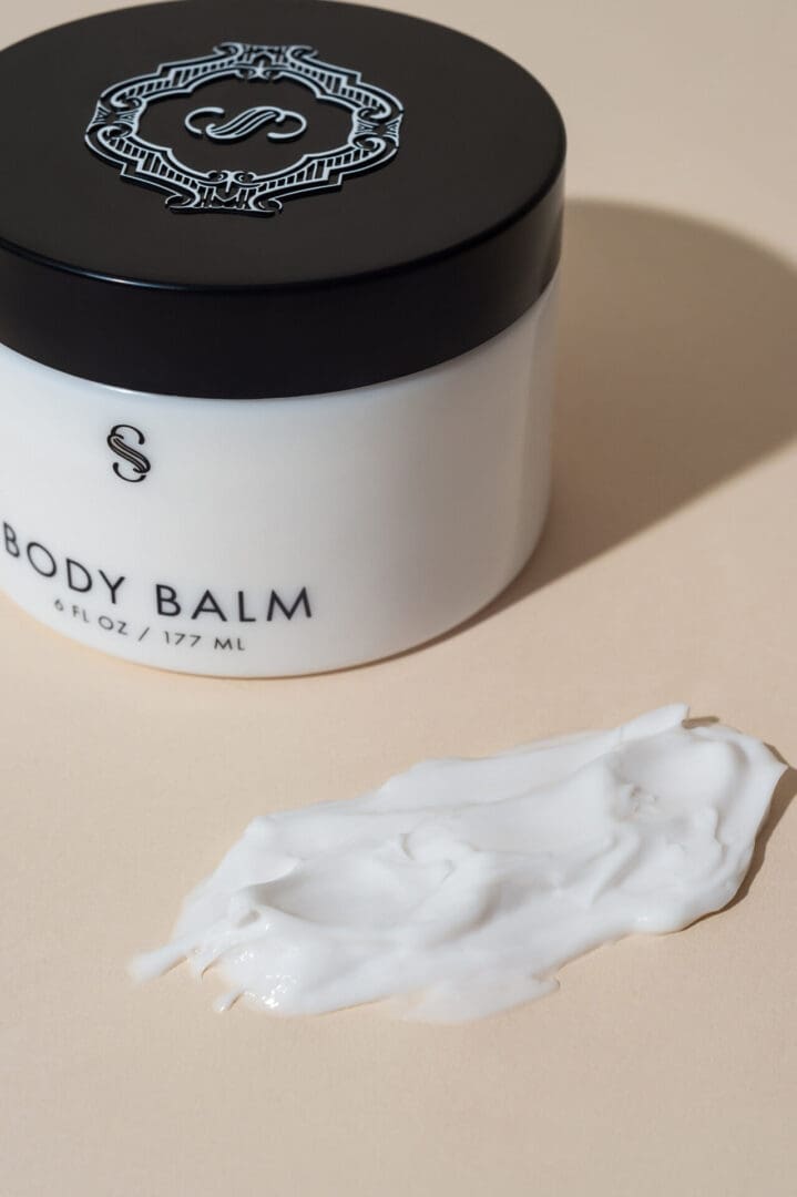 A white jar of body balm sitting on top of a table.