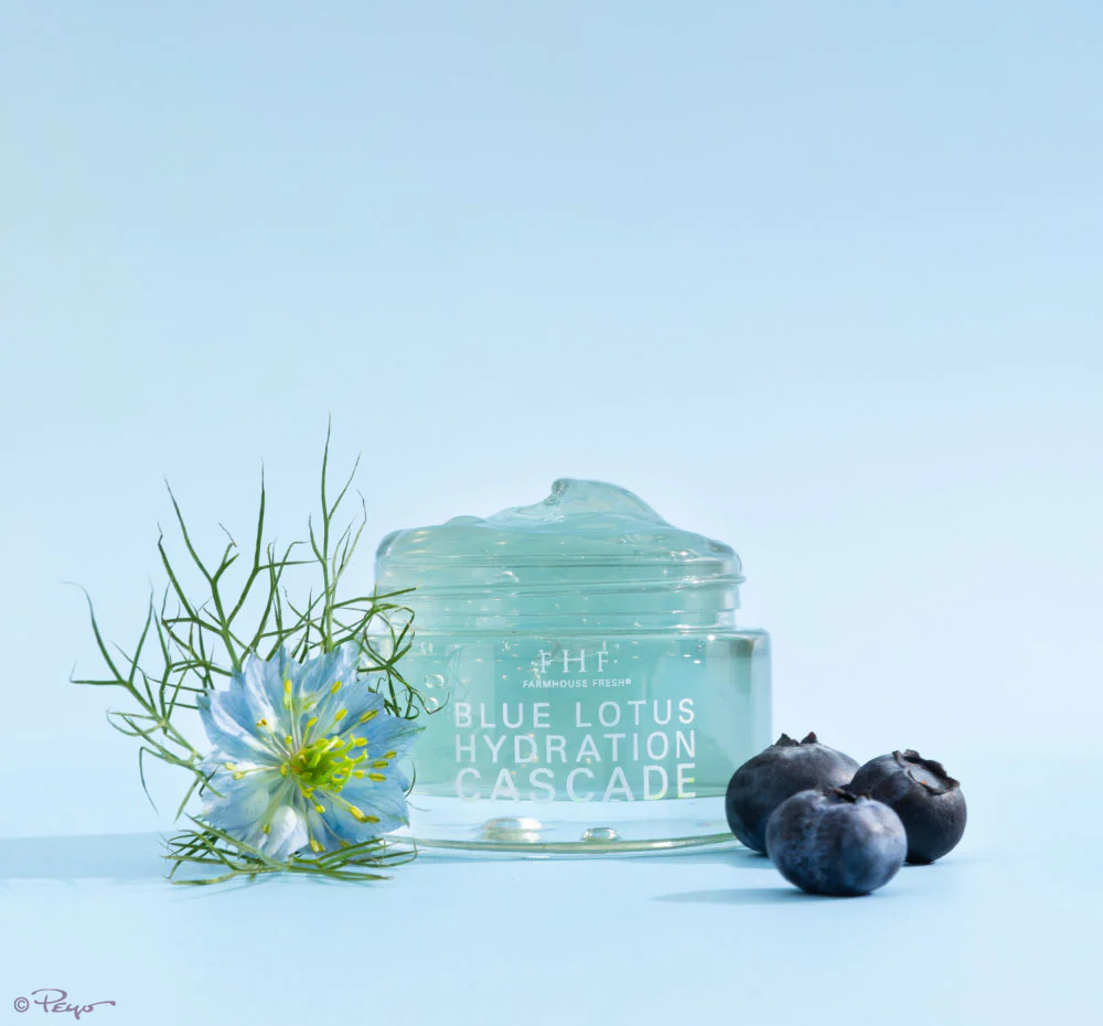 A jar of blue lotion next to some blueberries and a flower.